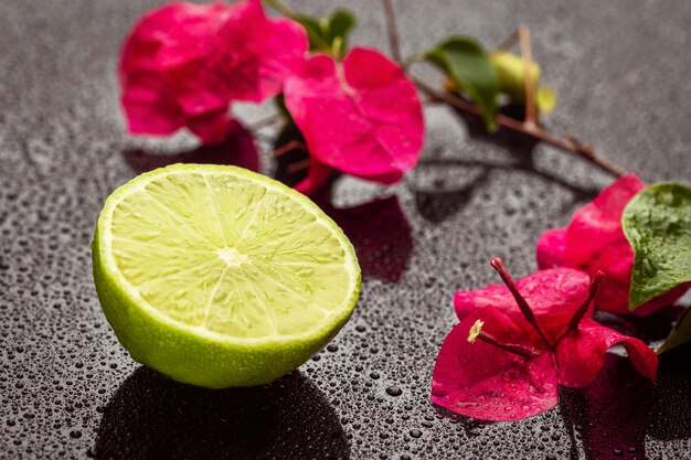 Medio lima fresca y flores rosadas sobre una superficie húmeda. De cerca