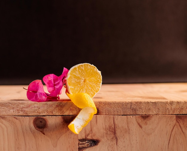 Foto medio limón con flores de color rosa sobre tabla de madera y fondo negro