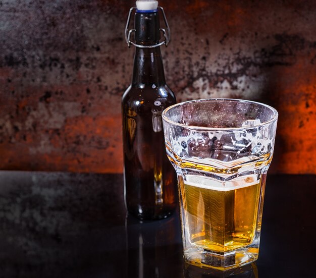 Medio vaso de cerveza y botella de cerveza sobre una superficie de espejo negro. Concepto de alimentos y bebidas