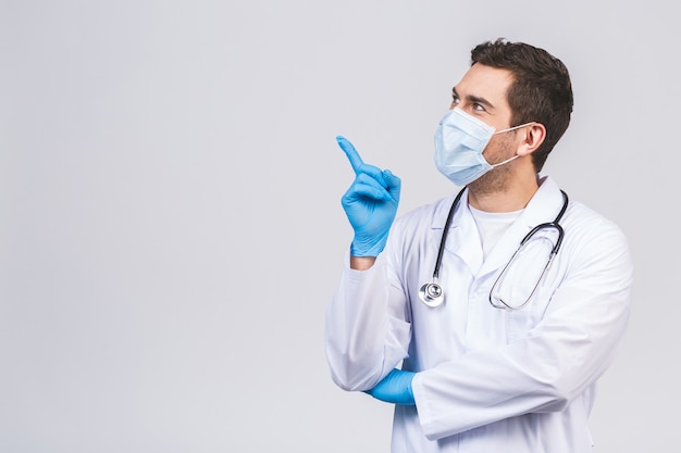 Medique o homem nas luvas estéreis da máscara protetora do vestido médico isoladas na parede branca. Epidemic pandemic coronavirus 2019-ncov sars covid-19 vírus da gripe. Apontando o dedo para cima.