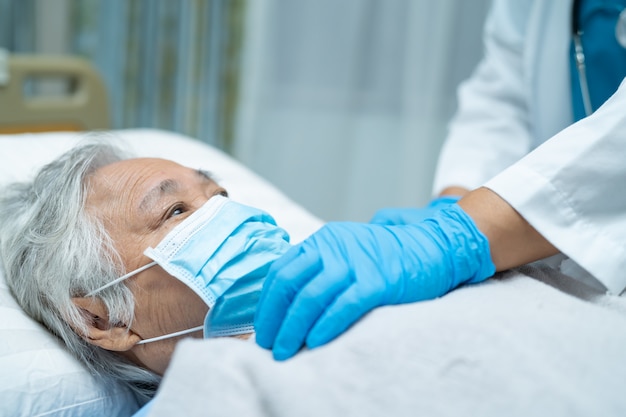 Medique usando o estetoscópio para verificar o paciente asiático sênior da mulher que veste uma máscara protetora