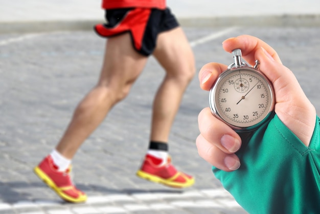 Foto medir la velocidad de carrera de un atleta usando un cronómetro mecánico. mano con un cronómetro en el fondo de las piernas de un corredor