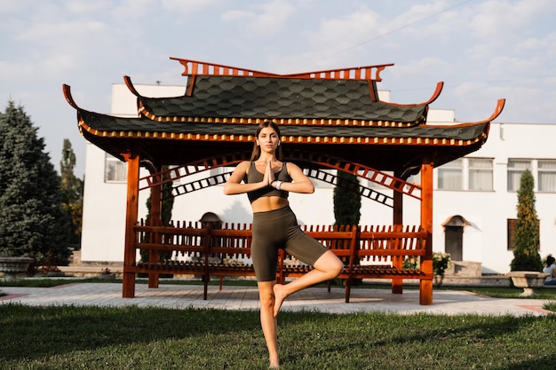 Meditação chinesa de qigong e treinamento esportivo ao ar livre Garota asiática adequada está meditando ao ar livre perto do caramanchão chinês