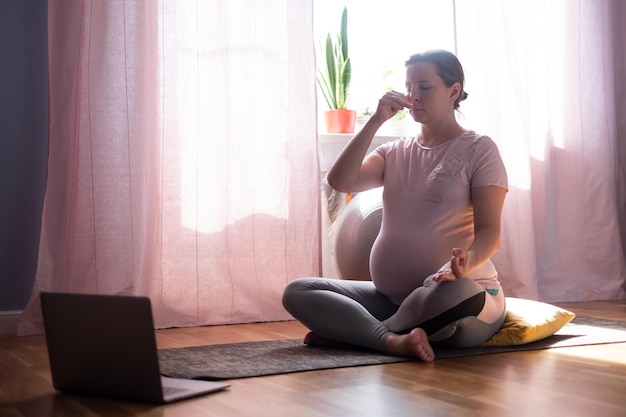 Meditação de ioga de gravidez. Mulher grávida saudável de comprimento total fazendo exercícios de ioga em casa. Posições de alongamento das mãos.