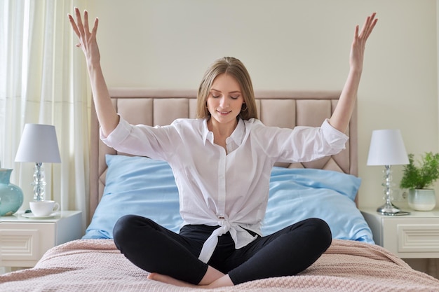 Meditação de ioga jovem linda loira sentada em posição de lótus na cama