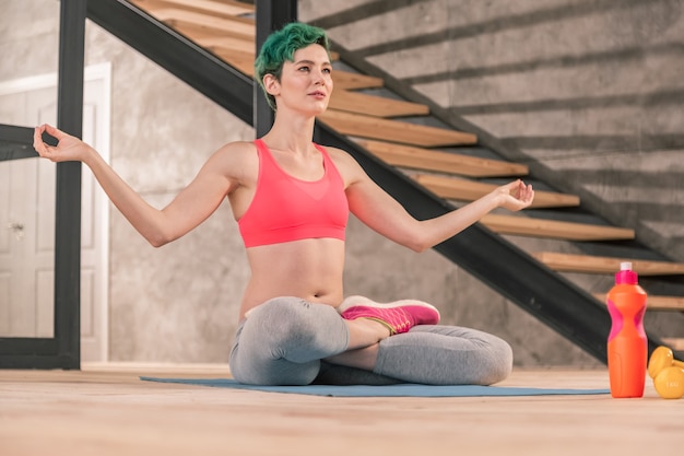 Meditación en casa. Atractiva meditación joven de pelo verde después de yoga matutino en casa