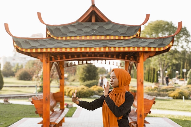 Meditación china Qigong y entrenamiento deportivo al aire libre. La mujer musulmana negra está meditando al aire libre cerca del cenador chino.