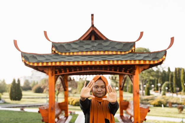 Meditación china Qigong y entrenamiento deportivo al aire libre. La mujer musulmana negra está meditando al aire libre cerca del cenador chino.