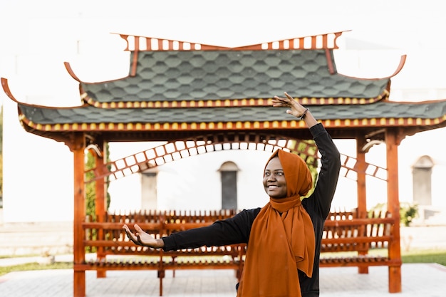 Meditación china Qigong y entrenamiento deportivo al aire libre. La mujer musulmana negra está meditando al aire libre cerca del cenador chino.