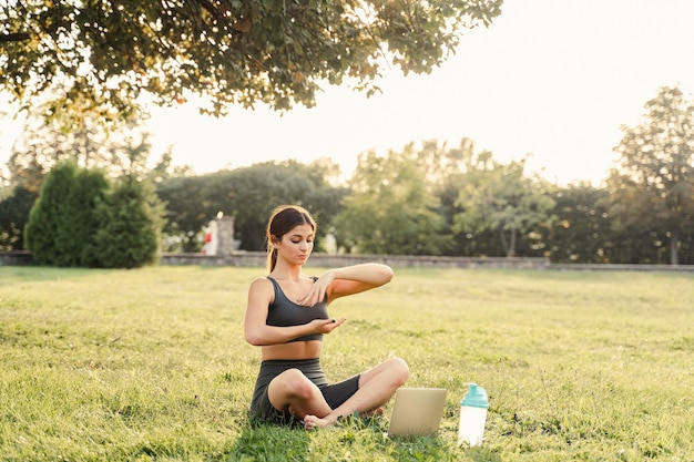 Foto meditación china qigong en línea con una computadora portátil en un parque verde entrenamiento deportivo al aire libre una chica asiática en forma está meditando afuera
