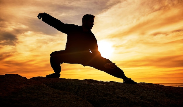 Meditación de hombre y entrenamiento de silueta y tai chi al aire libre en una playa bienestar y calma con fondo de puesta de sol Hombre oscuro y sombra con entrenamiento de artes marciales y meditación para una mentalidad de equilibrio