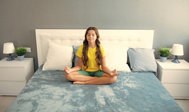 Meditación matutina en la cama Niño adolescente practicando meditación en el dormitorio Chica relajada en la cama en posición de loto y meditando yoga matutino en el dormitorio