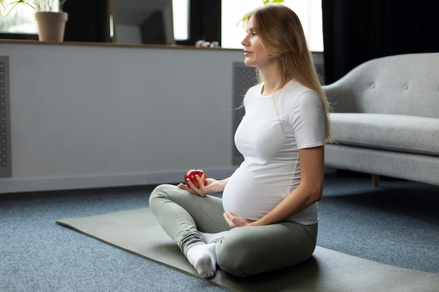 Meditación de mujer embarazada sentada con manzana roja en casa. Embarazo, concepto de comida saludable