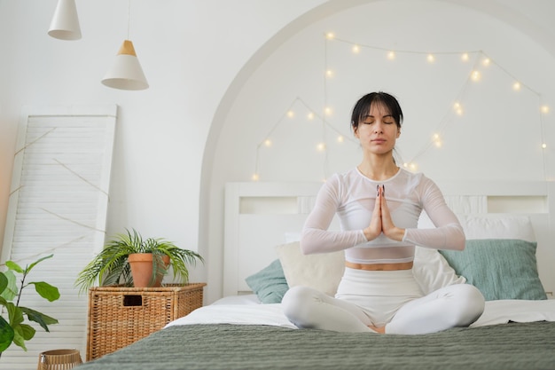 Foto meditación de yoga de atención plena mujer joven y sana practicando yoga en el dormitorio en casa mujer sentada en