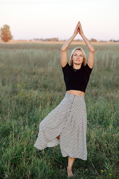 Meditando em um pé jovem loira se exercitando em um campo