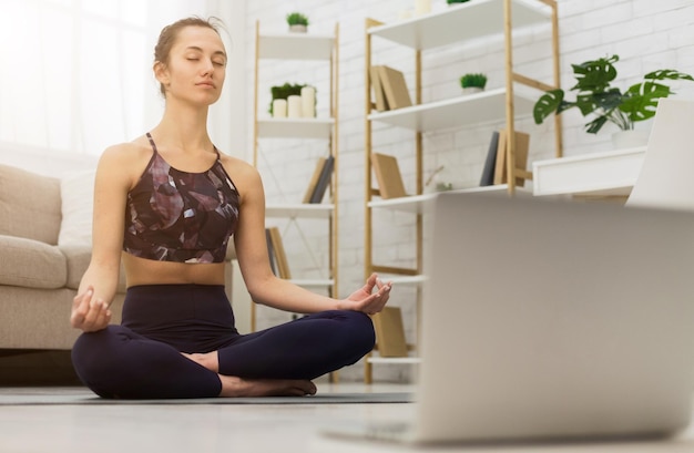 Meditando con laptop Mujer entrenando yoga en línea