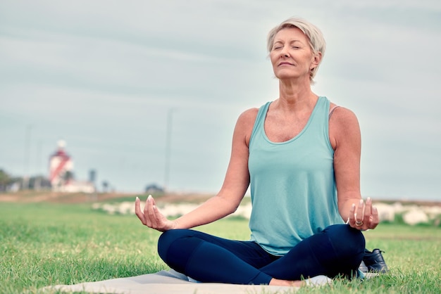 Meditation einer älteren Frau und Mudra-Übungen im Park für Wohlbefinden, geistige Gesundheit oder Fitness auf einem Himmelsmodell. Eine ältere Dame meditiert im Freien, um sich in einer friedvollen, heilenden Denkweise oder mit Zen-Händen beim Yoga-Training zu entspannen