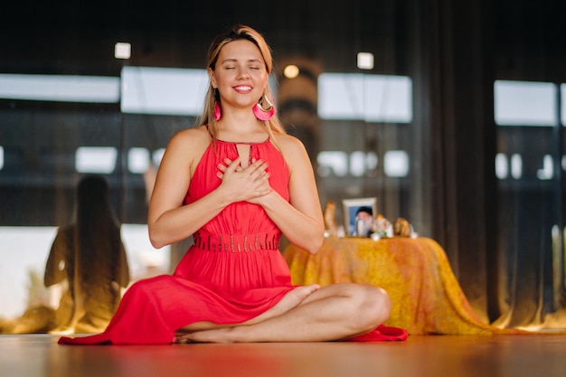 Meditation und Konzentration Eine Frau in einem roten Kleid, die mit geschlossenen Augen auf dem Boden sitzt, praktiziert drinnen Medizin. Ruhe und Entspannung