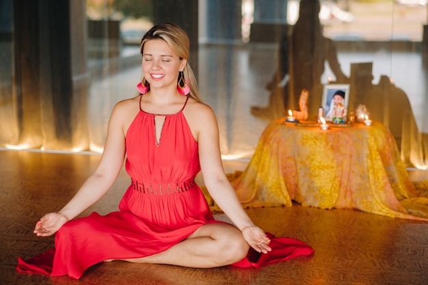 Meditation und Konzentration Eine Frau in einem roten Kleid, die mit geschlossenen Augen auf dem Boden sitzt, praktiziert drinnen Medizin. Ruhe und Entspannung