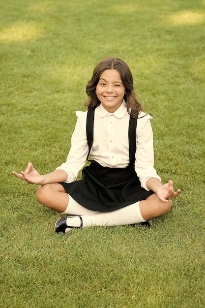 Meditationspraxis Gute Stimmung Friedliche Meditation Lerne Meditationstechniken Mädchenschülerin sitzt auf dem Rasen Schalte ein für einen produktiven Tag Yogatraining Kid adorable schoolgirl meditate