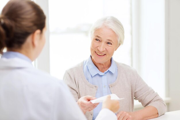 Medizin, Alter, Gesundheitswesen und Personenkonzept - Arzt verschreibt glücklicher Seniorin im Krankenhaus ein Rezept