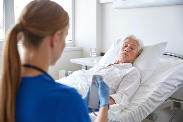 Foto medizin, alter, unterstützung, gesundheitsversorgung und personenkonzept - arzt oder krankenschwester, die das bett mit fernbedienung für ältere patientinnen auf der krankenstation anpassen