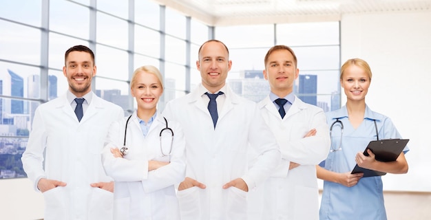 medizin, beruf, teamarbeit und gesundheitskonzept - gruppe lächelnder mediziner oder ärzte mit klemmbrett und stethoskopen über klinikhintergrund
