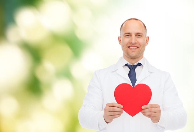Medizin, Beruf, Wohltätigkeits- und Gesundheitskonzept - lächelnder männlicher Arzt mit rotem Herzen auf natürlichem Hintergrund