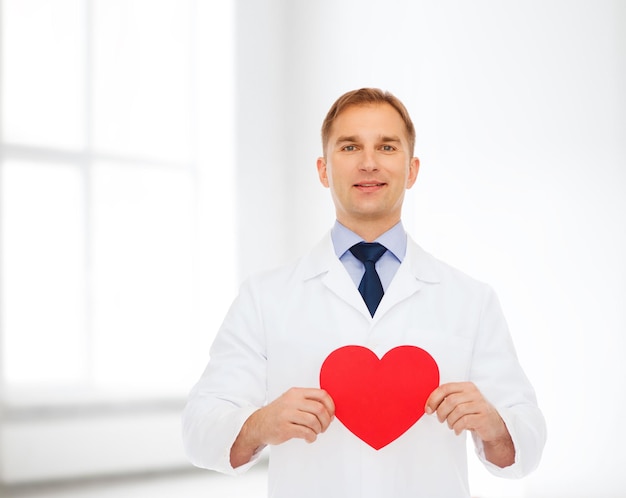 Medizin, Beruf, Wohltätigkeits- und Gesundheitskonzept - lächelnder männlicher Arzt mit rotem Herzen über weißem Raumhintergrund