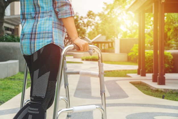 Medizin- und Gesundheitswesenkonzept, Frau, die mit einem Aluminiumwanderer an einem Park geht.