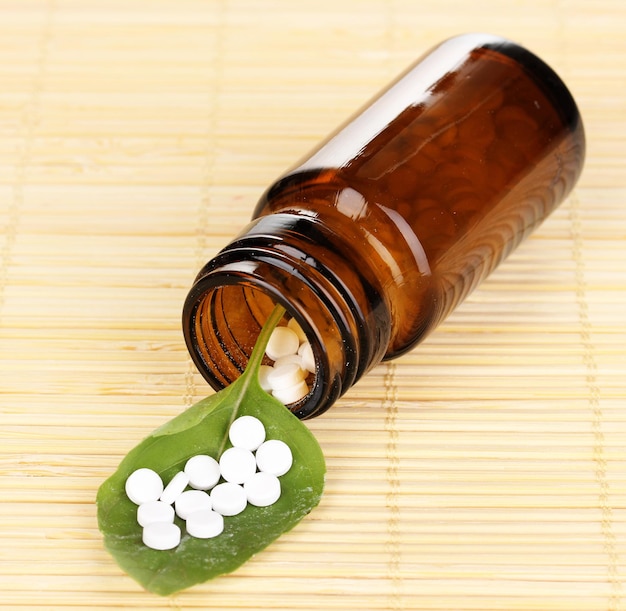 Medizinflasche mit Tabletten auf grünem Blatt auf Bambusmatte