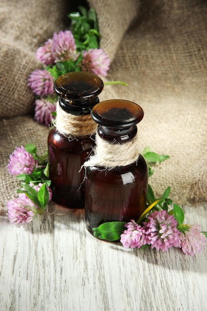 Medizinflaschen mit Kleeblumen auf Holztisch mit Sackleinen