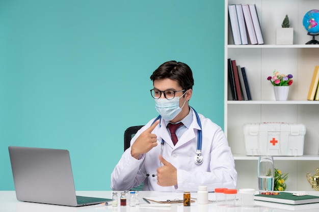 Medizinische Arbeit am Computer aus der Ferne ernster, süßer, intelligenter Arzt im Laborkittel, der auf Maske zeigt