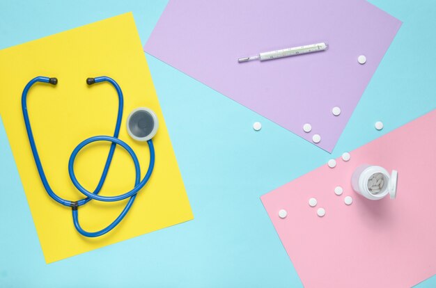 Medizinische Ausrüstung auf einem farbigen Papierhintergrund. Stethoskop, Thermometer, Flasche Vitamine. Medizinisches Konzept. Draufsicht