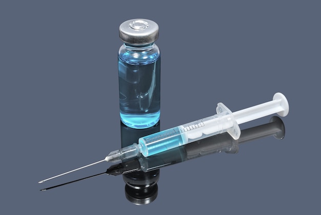 Medizinische Durchstechflasche mit blauem Impfstoff und Spritze im Dunkeln