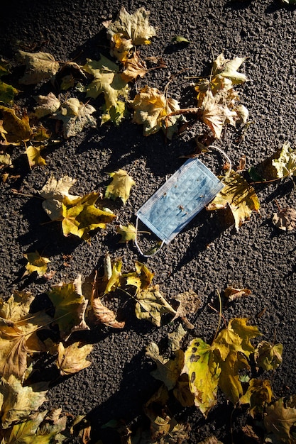 Medizinische Gesichtsmaske auf Asphalt liegend mit Herbstlaub im Freien