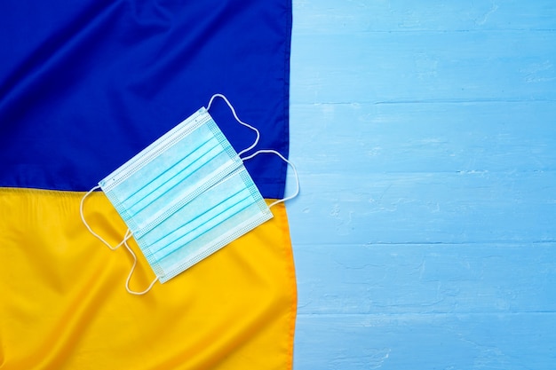 Medizinische Gesichtsmaske auf der Flagge der Ukraine auf Holzbrett