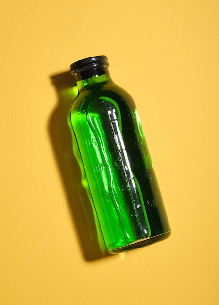 Medizinische Glasflasche mit grüner Flüssigkeit und hartem Schatten liegt auf gelbem Tisch Idee einer medizinischen Gesundheitszusammensetzung