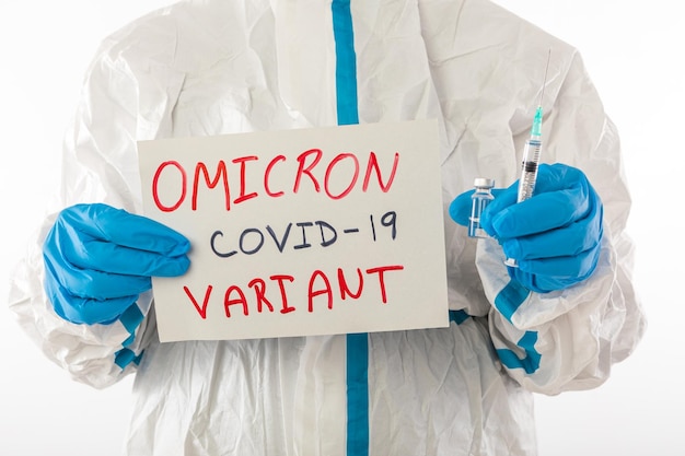 Medizinische Krankenschwester in PSA und Latexhandschuhen hält ein Schild mit der Aufschrift "OMICRON VARIANT COVID-19" und in der anderen Hand hält sie eine Nadel und ein Impffläschchen. Coronavirus, Pandemie und Gesundheitskonzept.