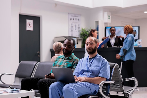 Medizinische Krankenschwester spricht mit männlichem Patienten über Diagnose und zeigt Krankheitsergebnisse auf Laptop in der Rezeptionslobby des Krankenhauses. Facharzt und Kranker unterhalten sich im Wartezimmer über Medikamente.