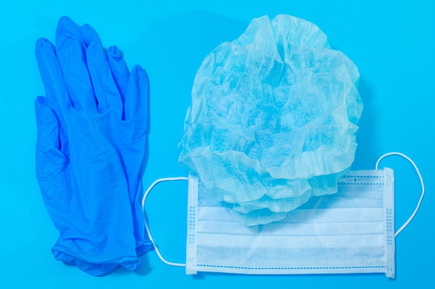 Medizinische Maskenhandschuhe und Hut auf blauem Hintergrund