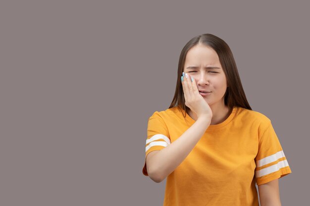 Medizinische Probleme und Krankheiten Schwere Zahnschmerzen Das Mädchen hält ihre Wange mit den Händen das Gefühl des Leidens auf ihrem Gesicht isoliert auf grauem Hintergrund