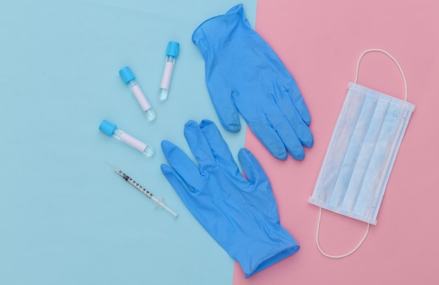 Medizinische Reagenzgläser mit Spritze und Gesichtsmaske, Handschuhe auf blauem rosa Pastellhintergrund. Impfung. Ansicht von oben