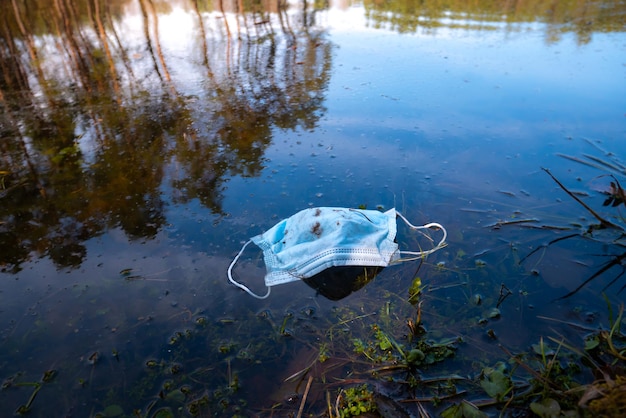 Medizinische Schutzmaske im Wasser des Stadtsees. Folgen des Coronavirus (COVID-19). Umweltverschmutzung, medizinisches Müllkonzept. Müll und Müll im Park.