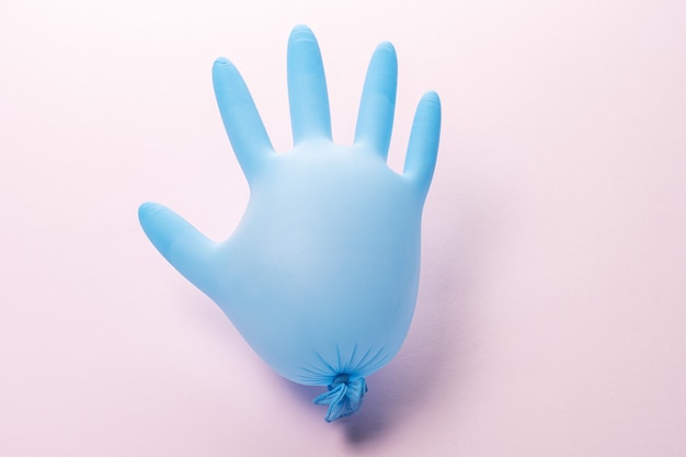 Medizinischer Handschuh des blauen Latex auf pastellrosa Hintergrund.