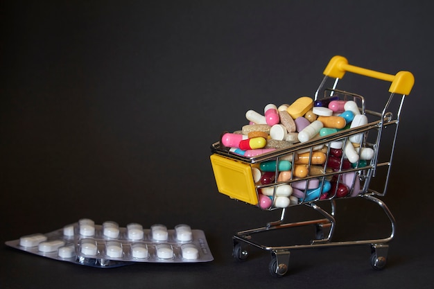 Medizinischer Hintergrund oder Konzept. Nahaufnahme eines Einkaufswagens gefüllt mit bunten Pillen. Wagen aus dem Supermarkt mit verschiedenen Medikamenten und Tablettenblister