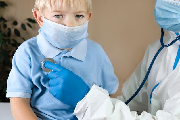 Medizinischer Untersuchungsjunge in der Klinik Kleines Kind vom Arzt untersucht Kinderarzt mit Stethoskop mit Gesichtsmaske und Kleinkind in einem Krankenhaus Überprüfen Sie die Herzlunge des Kindes Pädiatrische Untersuchung im Krankenhaus