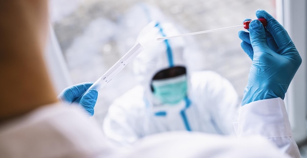 Medizinisches Fachpersonal in Schutzkleidung nimmt COVID19-Tupfer-Reagenzglas-Kit im Covid19-Testzentrum während des PCR-DNA-Testprotokollprozesses für Coronavirus-Epidemie