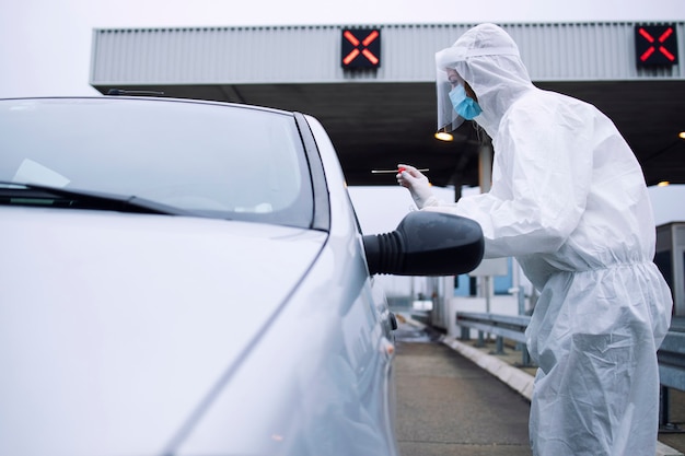 Medizinisches Gesundheitspersonal im schützenden weißen Anzug mit Handschuhen und Gesichtsmaske, die einen Nasen- und Rachenabstrich nimmt, um den Passagier aufgrund des Koronavirus zu testen.