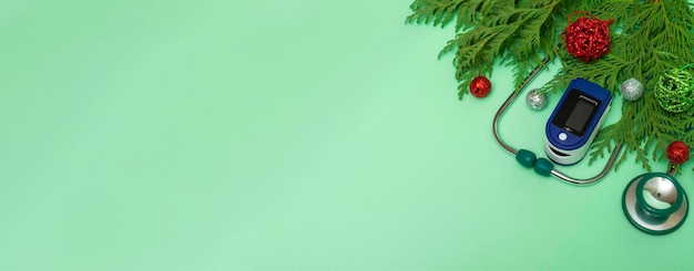 Medizinisches Konzept: Weihnachten im Gesundheitswesen feiern. Draufsicht auf eine flache Laiennahaufnahme eines Stethoskops, Pulsoximeter mit Tannenzweigen auf grünem Hintergrund. Mit Kopienraum. Banner